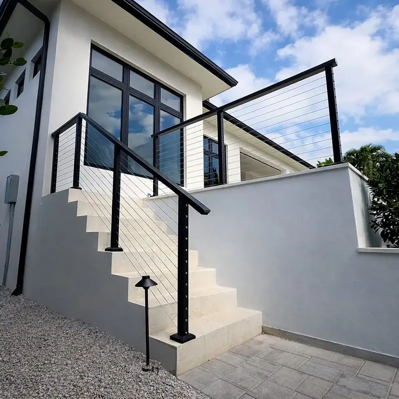 A view from the foot of the stairs shows black posts, a matching handrail and horizontal cables continuing around the raised terrace.