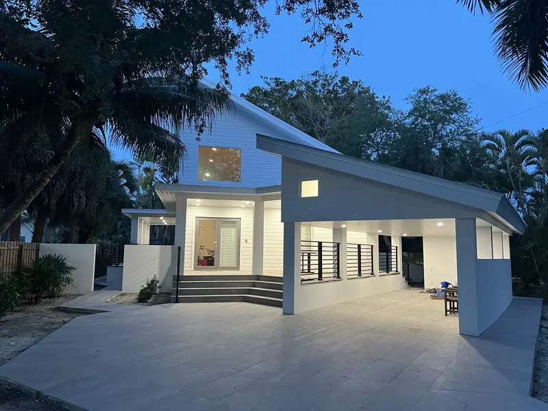 A dusk view of a modern home shows a covered driveway, square columns and dark horizontal accents along the entry.