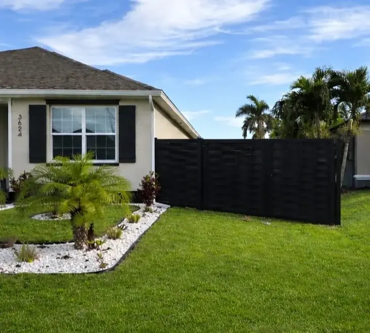 Dark privacy panels beside a front garden with white stones and shrubs.