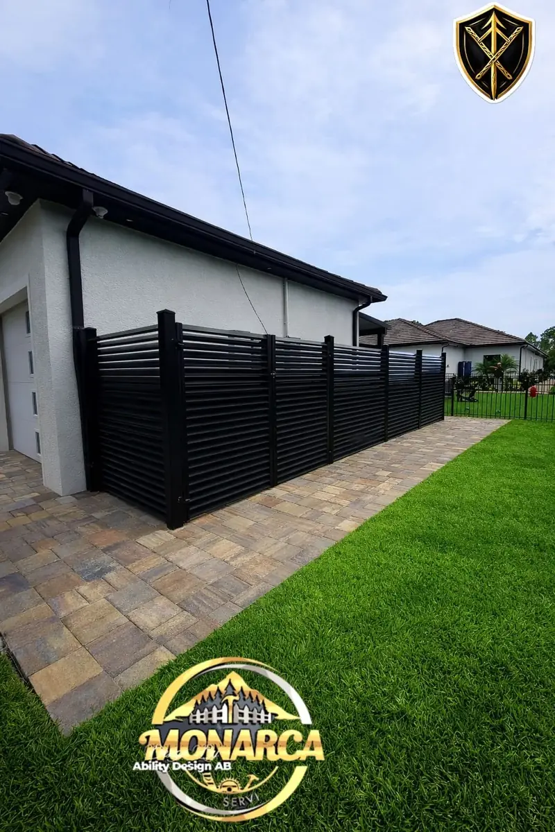 Tall black horizontal slats screen the side of the home beside a narrow paver walkway and landscaped lawn.