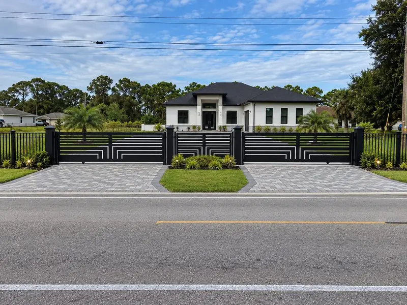 A geometric black double driveway gate at a landscaped entrance.