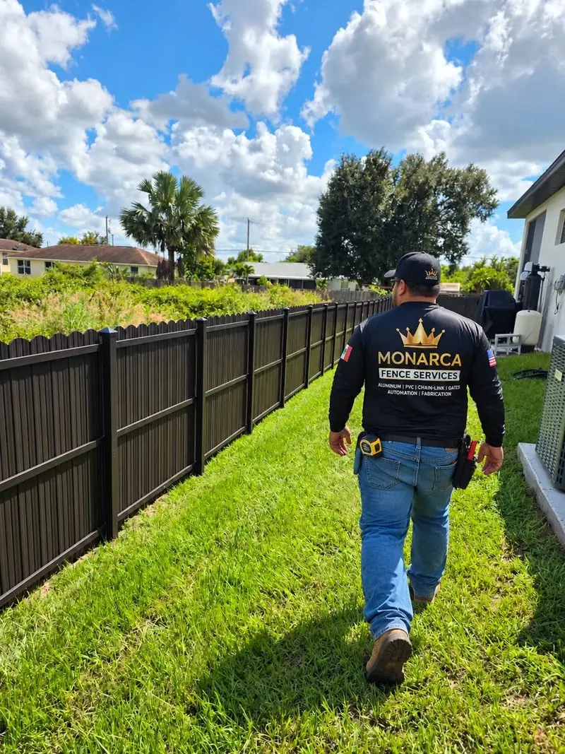 Monarca Fence Services team member walking beside a black fence installation