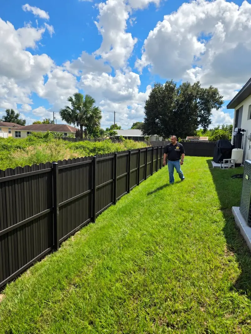 A wide view of the new dark privacy fence running the full depth of the yard beside the house.