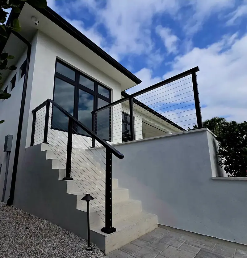 Black cable railing climbs the exterior concrete stairs and wraps the upper terrace of a modern white home.