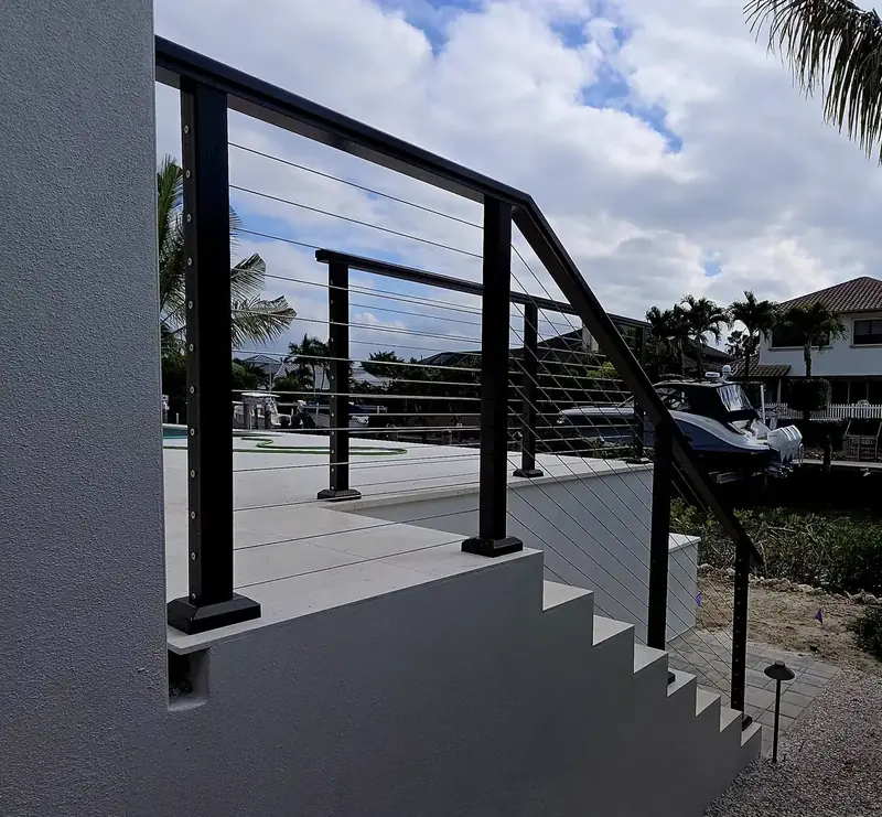 Black posts and a black top rail with horizontal stainless cables follow the exterior stairs and deck edge of a canal-front home.